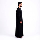 Qamis noir signature saoudien pour homme, vêtement traditionnel élégant, porté par un homme. MonQamisHomme.
